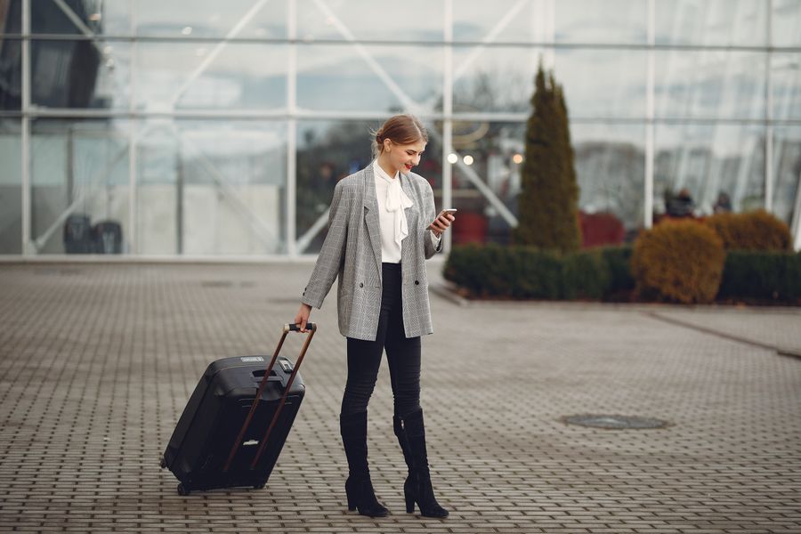 Una viaggiatrice con la valigia controlla il telefono all'uscita dell'aeroporto